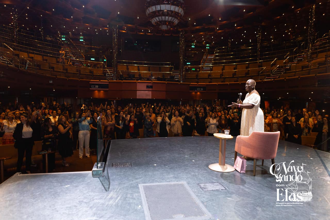 Mulher palestrando no palco diante da plateia durante edição anterior do Navegando com Elas